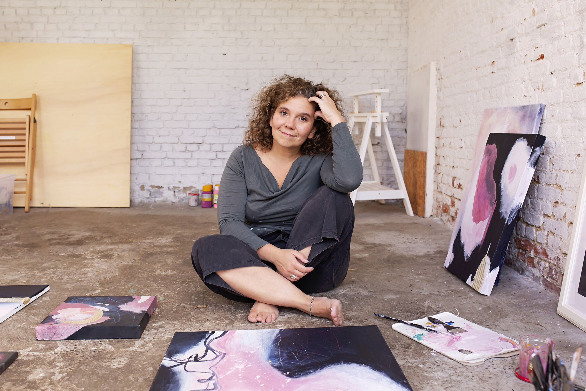 Mieke Fleurackers sitting on the floor of her studio surrounded by her abstract pink and black paintings